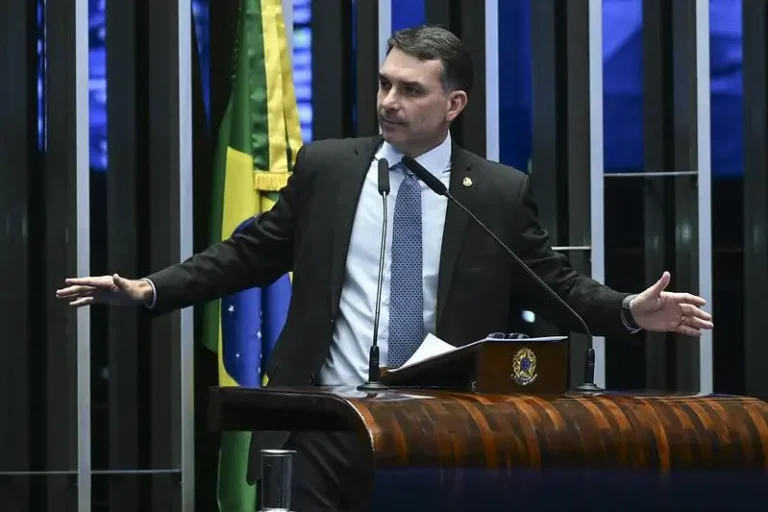 Flávio Bolsonaro discursa na tribuna do Senado Federal, diante de microfones e da bandeira do Brasil.